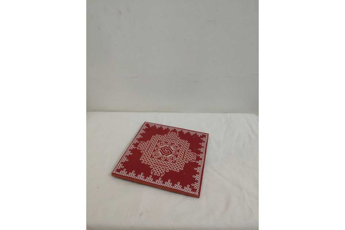 Close-up view of intricate white handpainted Kolam Rangoli art on red wooden pooja manai