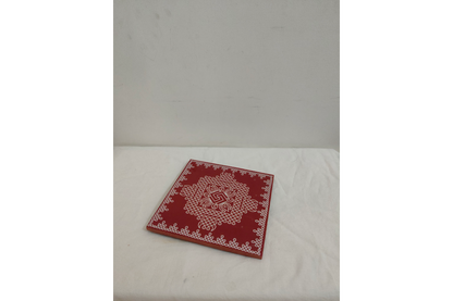 Close-up view of intricate white handpainted Kolam Rangoli art on red wooden pooja manai