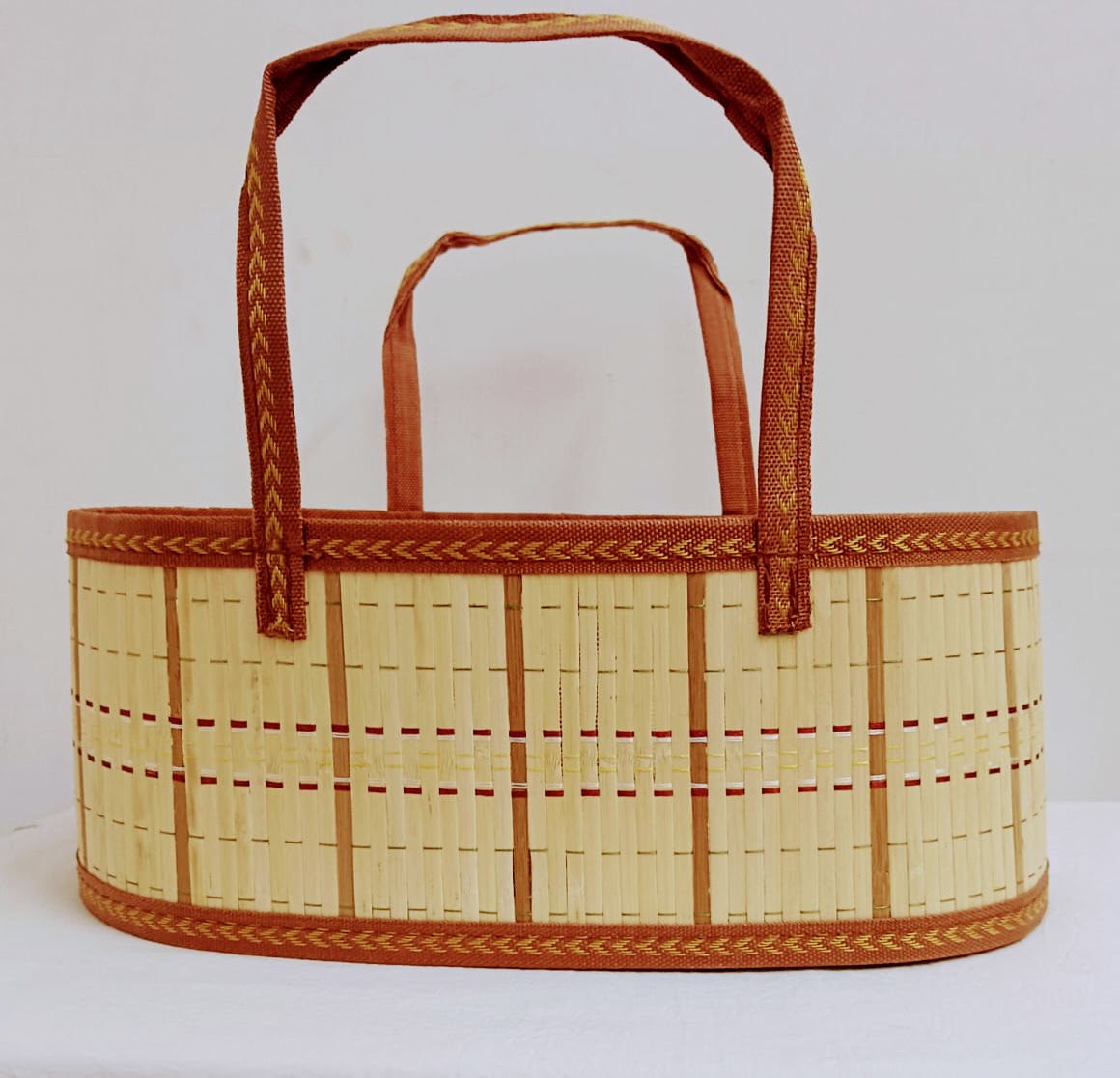 A woven straw basket tote bag with brown fabric handles and decorative braided trim, shown against a plain white background.