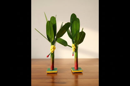 Two decorative plants with green leaves and yellow flowers on a white surface.