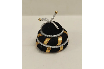 Decorative object resembling a beehive with black, gold, and white colors on a light gray background.
