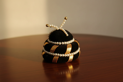 Decorative object resembling a bee with black, gold, and pearl accents on a wooden surface.