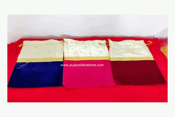 Three small drawstring pouches with gold trim are laid side by side on a bright red cloth.