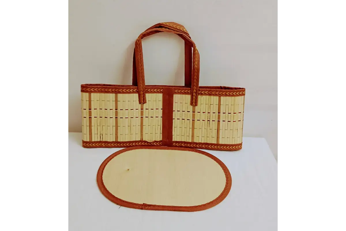 A woven straw tote bag with brown leather handles and trim, displayed next to an oval matching leather pad on a white surface against a plain light background.