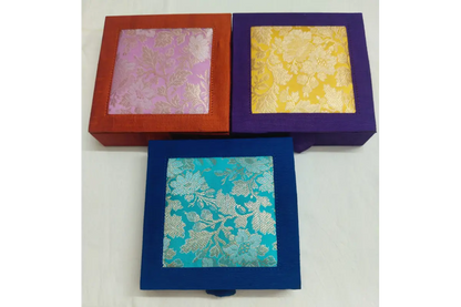 Three square decorative boxes with woven floral brocade fabric lids, shown in red-orange, purple, and blue frames on a white background.
